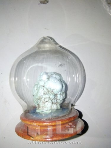 حجر فيروز موضوع داخل حافظه زجاجية بقاعدة خشب